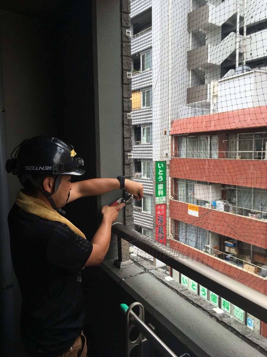三郷市の鳩駆除:ベランダの端で鳩よけネットを取り付ける作業